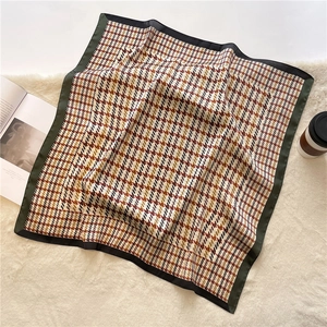 Detail of elegant houndstooth silk scarf with dark green trim on a soft beige background