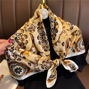 Detail of vintage paisley silk scarf in yellow and brown tied on a floral gold hanger