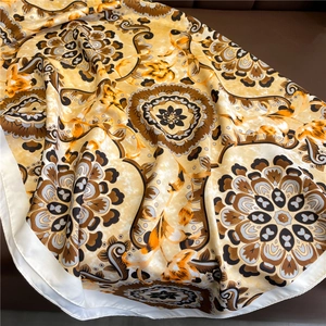 Detail showing the silky texture and golden baroque pattern of the square headscarf