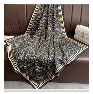 Détail d'un foulard carré en soie avec motifs floraux dorés sur un canapé en cuir