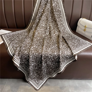 Carré de soie marron à motif floral et bordure rayée posé sur un canapé en cuir