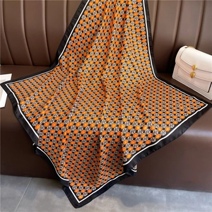 Detailed texture of a 90cm silk scarf with orange floral patterns on a leather sofa