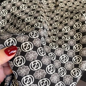 Close-up of black silk scarf featuring twill texture and floral monogram patterns