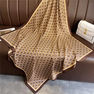 Detail view of a 90cm silk scarf with floral patterns on a leather sofa with accessories