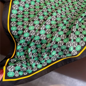 Detail of silk scarf showing green clover patterns and yellow trim with a soft drape