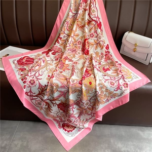 Détail du carré de soie rose avec motifs floraux vintage sur un canapé en cuir