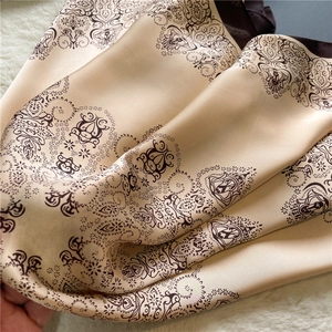 Close-up of champagne gold paisley silk scarf texture on white plush background