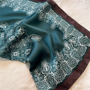 Detail of silk-like dark green scarf with white mandala patterns and brown borders
