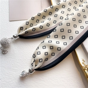 Détail d'un foulard en soie crème avec imprimé trèfle et pendentifs en argent sertis
