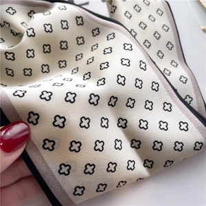 Gros plan du foulard en soie crème avec motif de trèfle noir et bordures contrastées