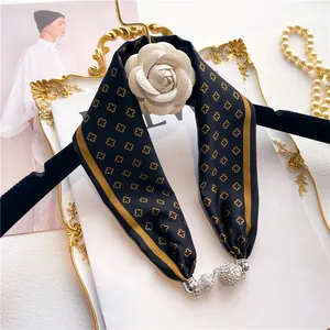 Détail d'un foulard en soie avec fleur de camélia et pendentif strass sur plateau doré