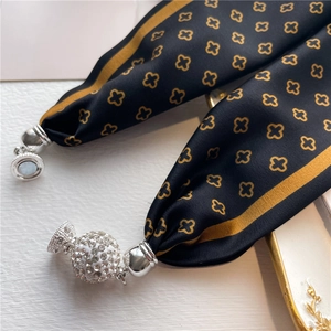 Détail d'un foulard en soie noire à motifs trèfles dorés et pendentif boule de strass chic