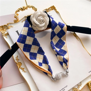 Détail d'un foulard en soie à losanges bleu et beige avec fermoir magnétique argenté