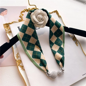 Détail d'un foulard en soie à carreaux vert-beige avec camélia blanc et perle argentée