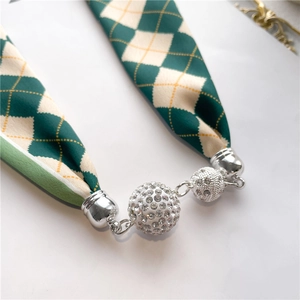 Détail du fermoir magnétique serti de diamants et du foulard en soie à carreaux verts