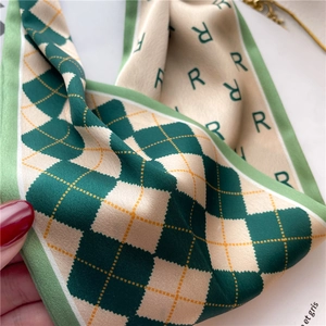 Vue macro d'un foulard en soie à motif losanges vert et beige avec lettrage R et texture fine