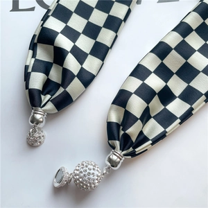 Détail macro du foulard en soie à damier avec fermoir magnétique et pendentif strass