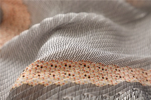 Détail du tissu plissé d'un foulard en soie au motif à carreaux orange, noir et blanc
