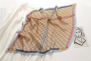 Détail d'un foulard plissé en soie avec motifs de chaînes dorées et bleues sur tissu blanc