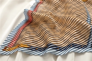 Détail d'un foulard plissé en soie avec motifs en damier beige et bleu et monogrammes
