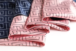 Detail of silk-like satin scarf featuring geometric maze patterns in navy and pink