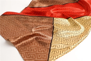 Close-up of geometric pattern satin scarf with red and gold color blocking detail