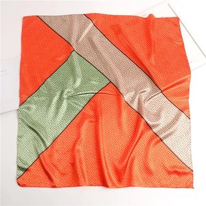 Macro detail of geometric satin silk square scarf with orange and mint green patterns
