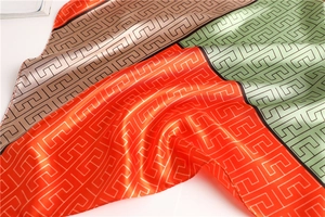Detailed macro shot of satin scarf featuring geometric Greek key patterns and color blocking