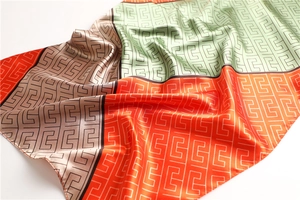 Macro detail of satin silk scarf showing interlocking G geometric pattern and colorful stitching