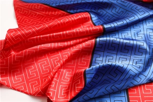 Detail of satin scarf showing geometric monogram pattern and red-blue color blocking texture