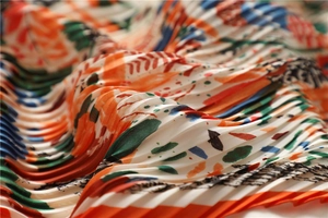 Dettaglio di un foulard in seta plissettata arancione con stampa astratta e texture