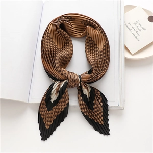 Macro detail of pleated silk scarf with coffee geometric checks on a minimal white book