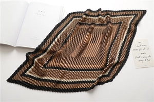Close-up of pleated silk scarf with brown and beige geometric patterns on white desk