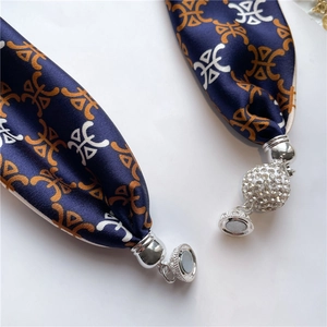 Dettaglio di sciarpa in seta blu navy con motivi geometrici e chiusura magnetica con strass