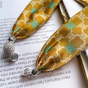 Dettaglio di un foulard in seta giallo con chiusura magnetica a strass su rivista