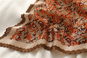 Detail of pleated geometric scarf fabric with orange and brown accordion texture folds