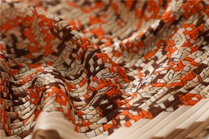 Macro view of geometric pleated silk scarf featuring orange and brown color blocks