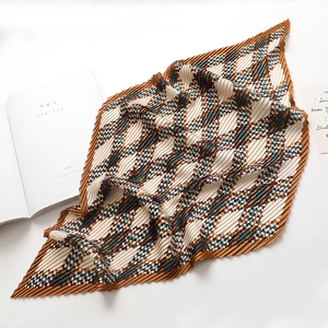 Detail of pleated silk scarf with brown and green houndstooth pattern on white surface