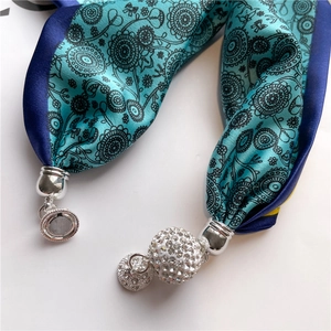 Détail d'un foulard en soie bleu canard avec breloques en strass et fermoir magnétique argenté
