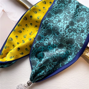 Détail d'un foulard en soie avec motifs de poissons, fleurs et un pendentif boule argenté
