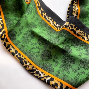Détail d'un foulard en soie verte avec bordures orange et motifs léopard et floraux