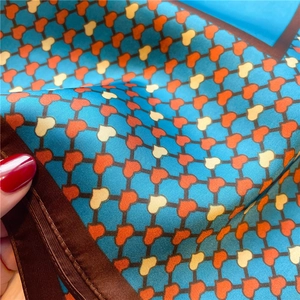 Detail of teal satin scarf featuring orange heart grid patterns and brown borders