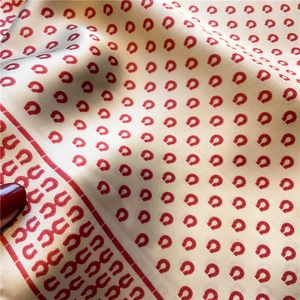 Detail eines Seidenschals in Champagner mit roten Hufeisenmustern und Seidenglanz