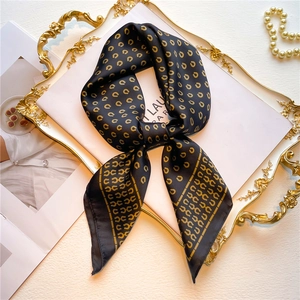 Detail eines eleganten Seidentuchs in Schwarz und Gold mit Hufeisenmuster auf Tablett