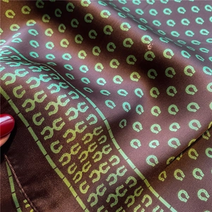 Detail eines Satin-Seidenschals mit grünem Hufeisenmuster auf tiefbraunem Stoff