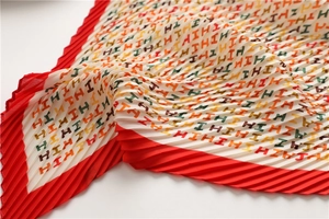 Close-up of pleated silk scarf featuring colorful H letter patterns and red borders