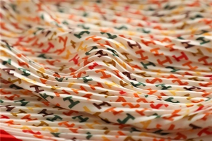 Close-up of pleated silk scarf with colorful H letter pattern and fine folded texture