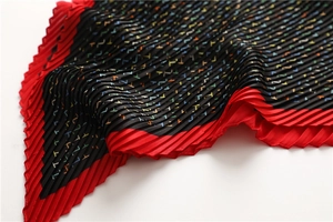 Detail of pleated scarf showing black fabric with red accordion edges and H pattern
