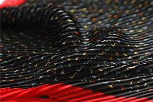 Detailed macro view of pleated fabric showing colorful geometric H patterns on a scarf