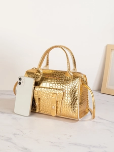 Goldene Handtasche mit Krokodilprägung neben Smartphone zur Größenveranschaulichung